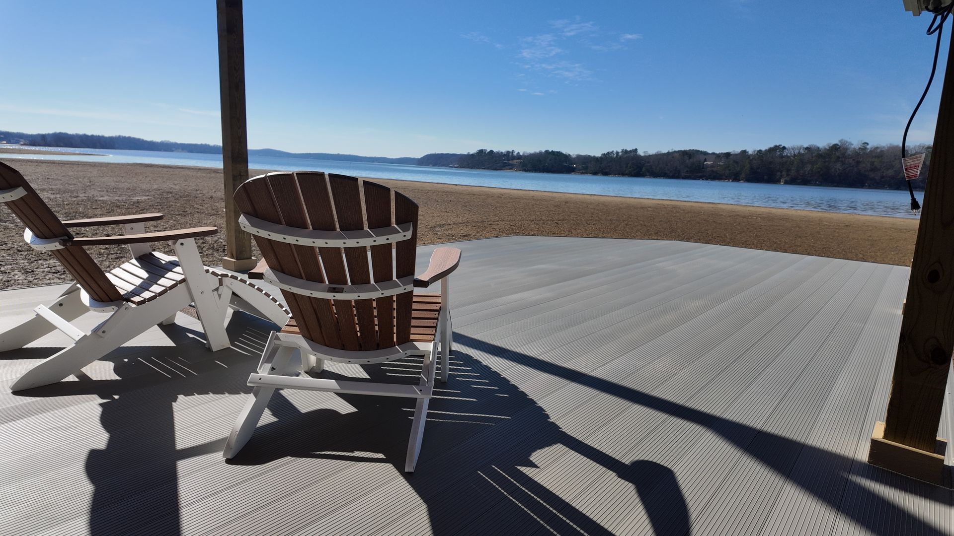Adirondack chairs on a wooden dock overlooking calm blue water under a clear sky.
