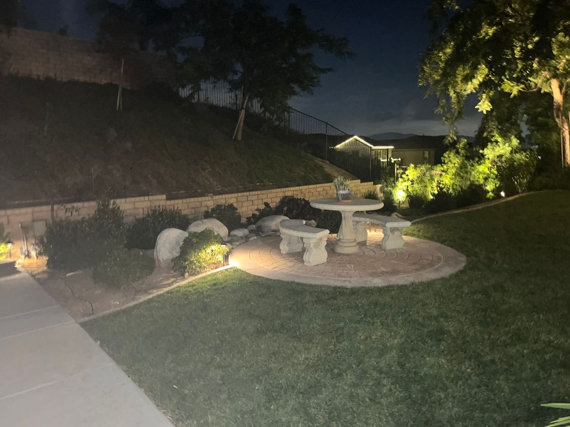 A picnic table and benches are lit up at night in a backyard.