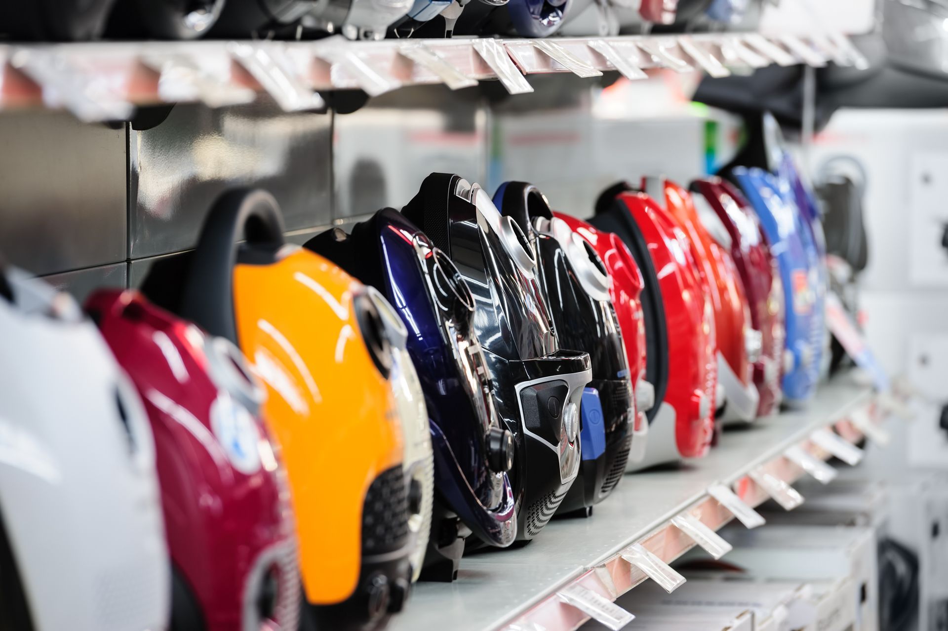 A row of vacuums are lined up on a shelf in a store.