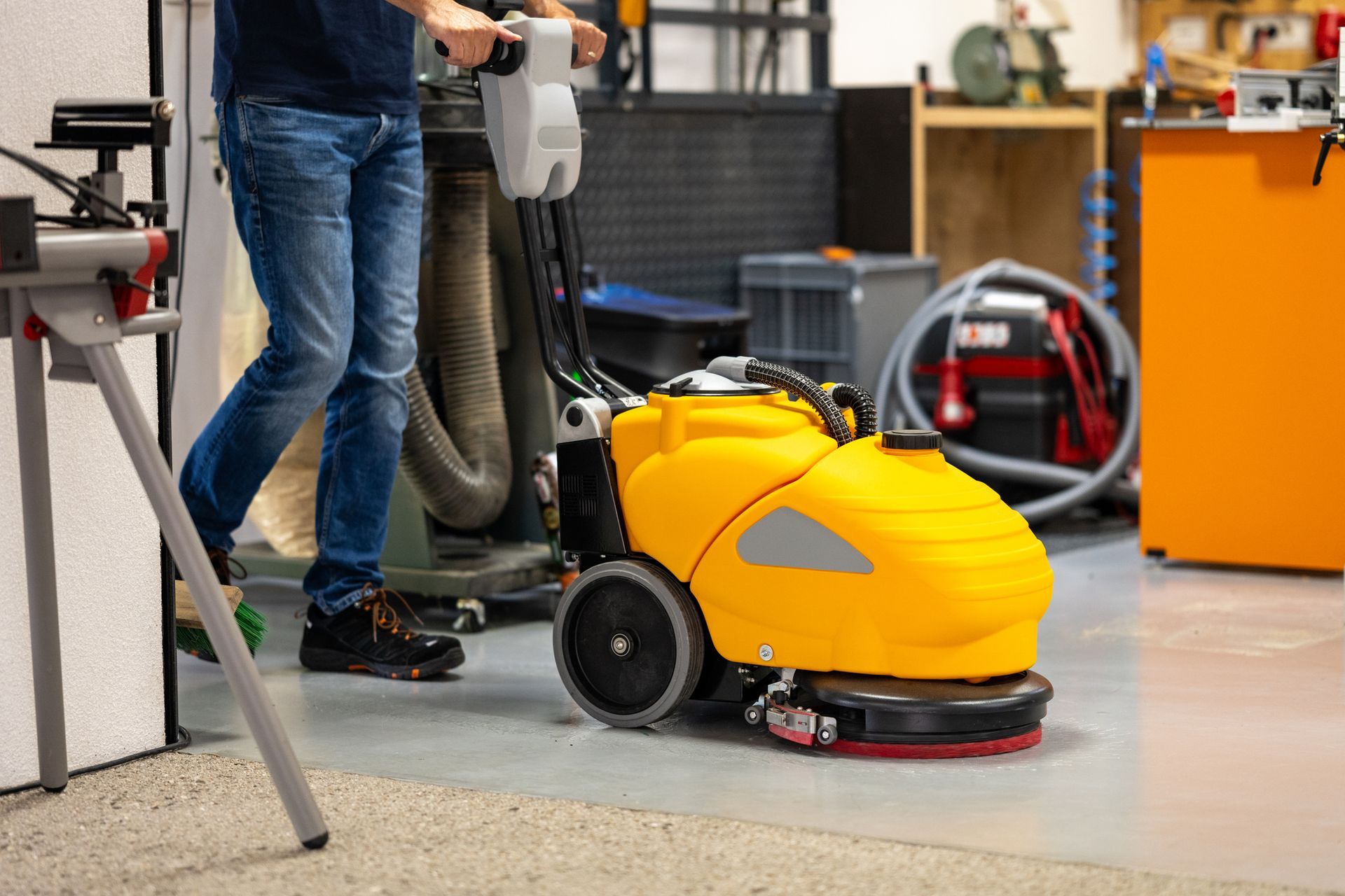 A man is cleaning the floor with a machine in a garage.