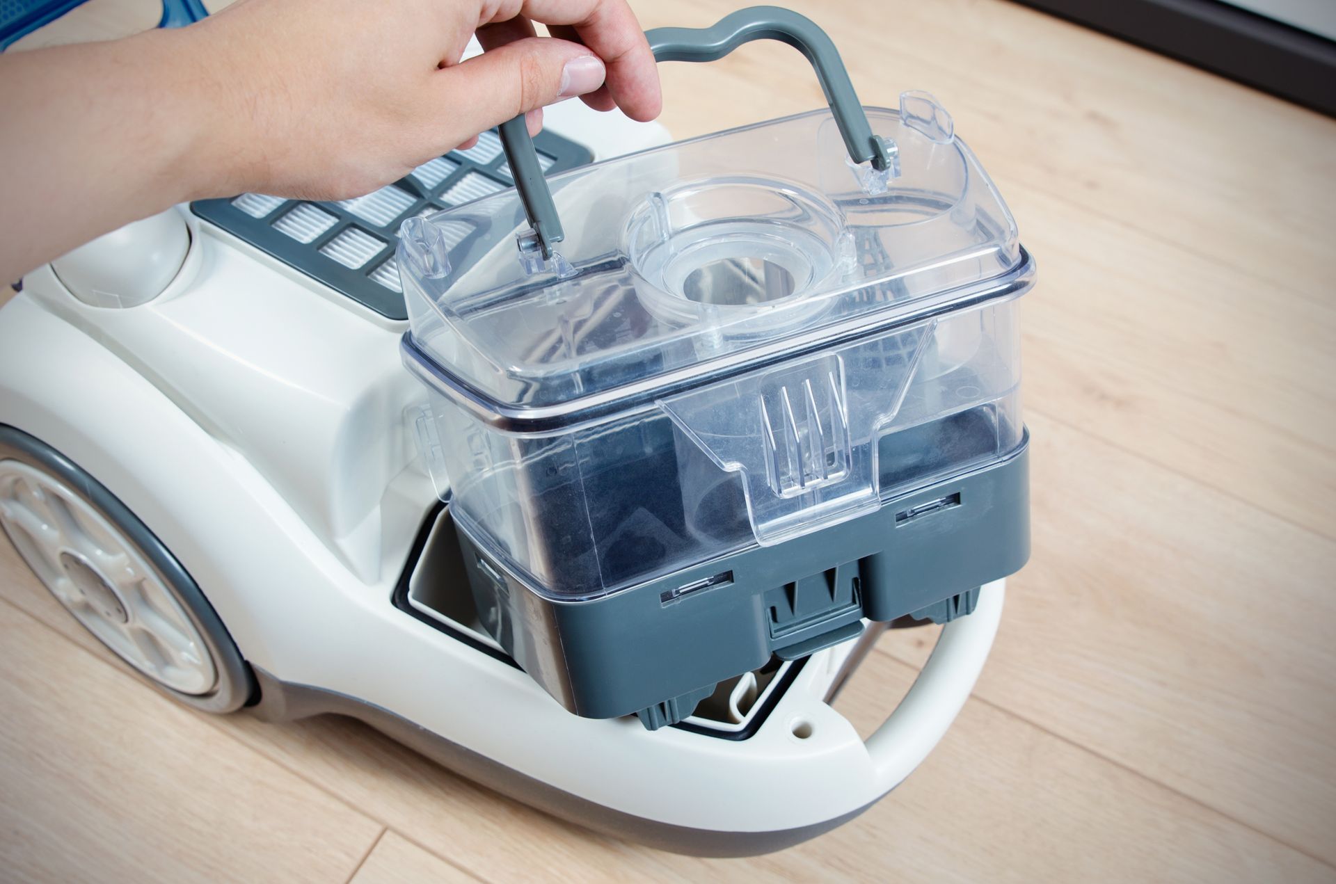 Hand removing water tank from carpet cleaning machine on wooden floor.