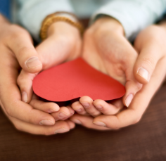 A person is holding a red heart in their hands