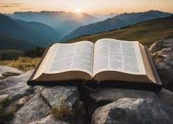 An open bible is sitting on top of a rocky hill with mountains in the background.
