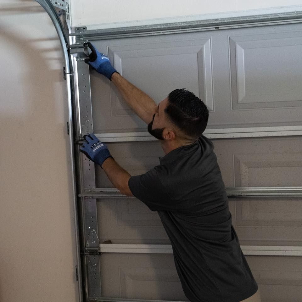 A man wearing blue gloves is working on a garage door.