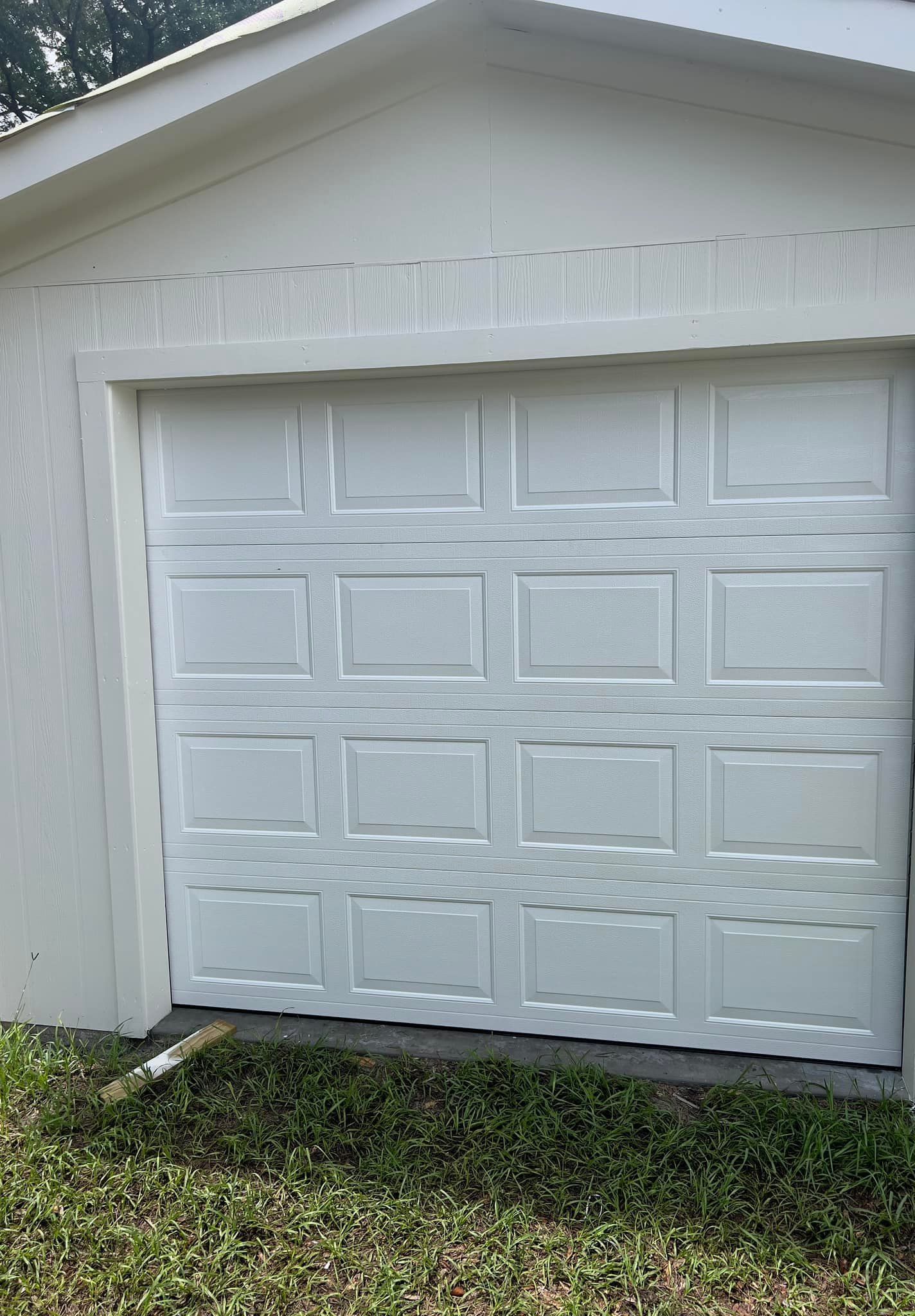 A white garage door is sitting in the grass next to a house.