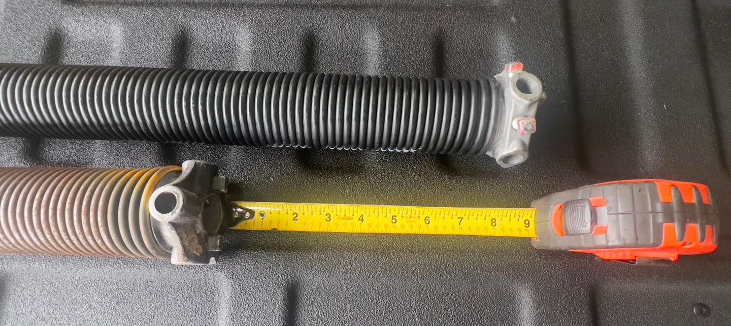 A garage door spring is being measured with a tape measure.