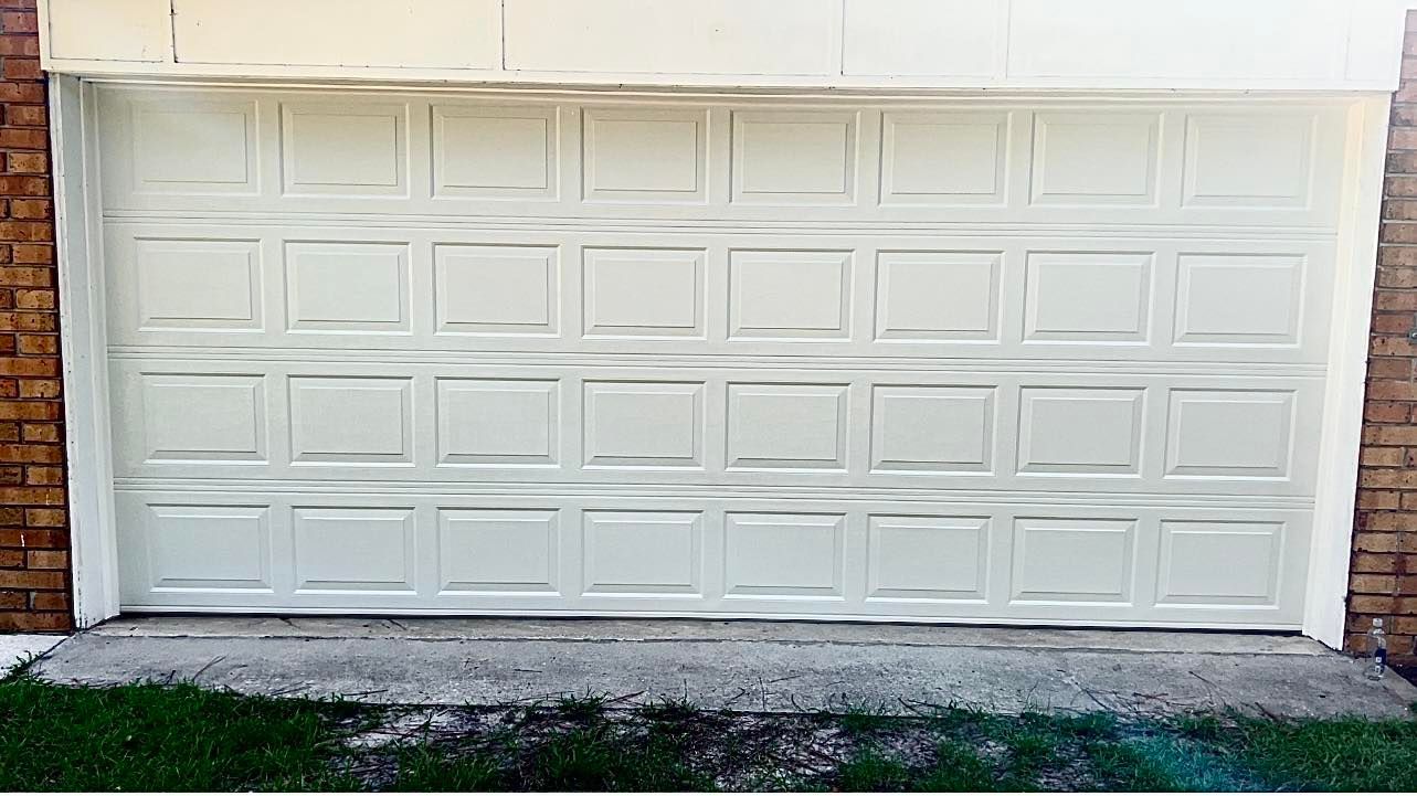 A white garage door is sitting in front of a brick building.