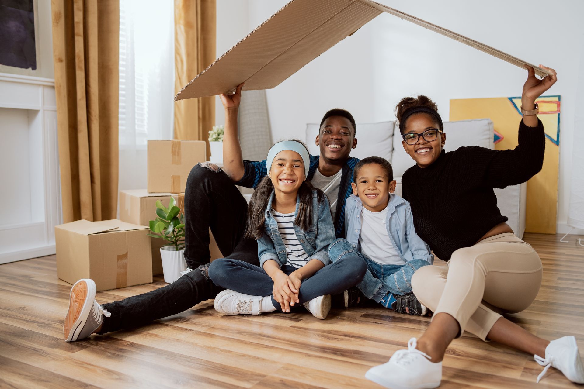 A family is sitting under a cardboard box in their new home.