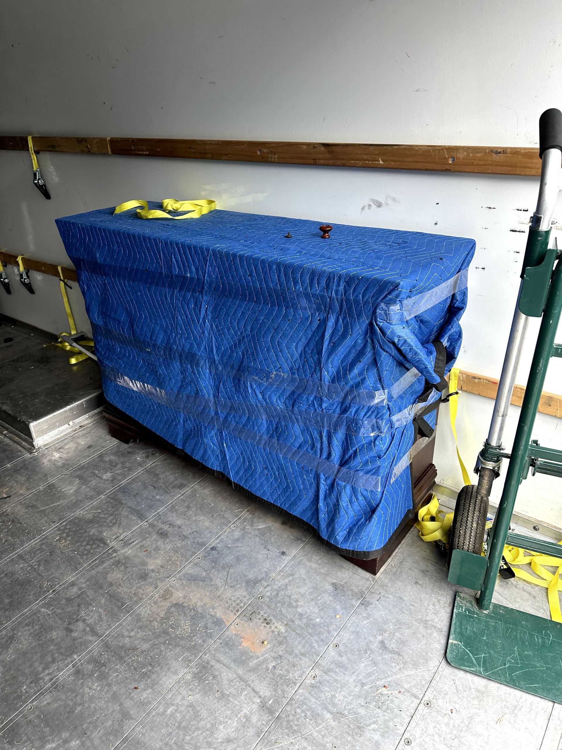 A blue tarp is covering a piano in a truck.