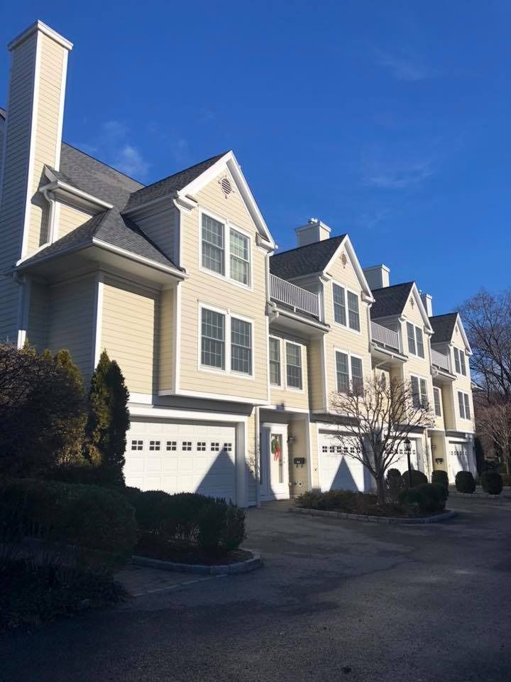A row of light yellow townhouses with dark shingled roofs and white garage doors under a clear blue sky.