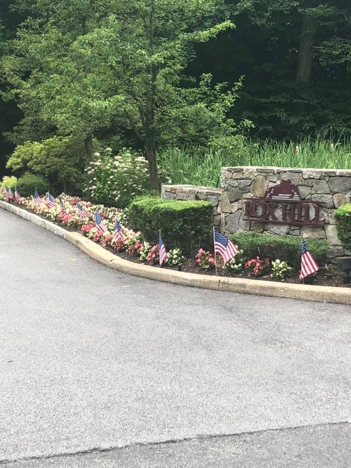 A stone entrance sign for Oak Hill, surrounded by landscaping decorated with many small American flags.
