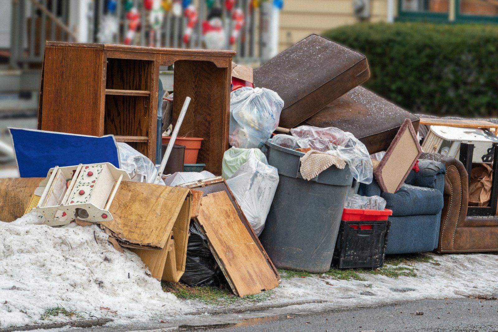 Pile of discarded furniture and trash on a snowy curb. Includes wood, cushions, and plastic bags.