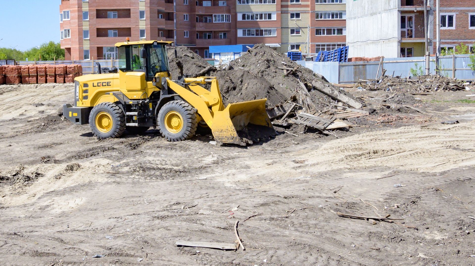 Yellow loader pushing dirt on a construction site, residential buildings in background.