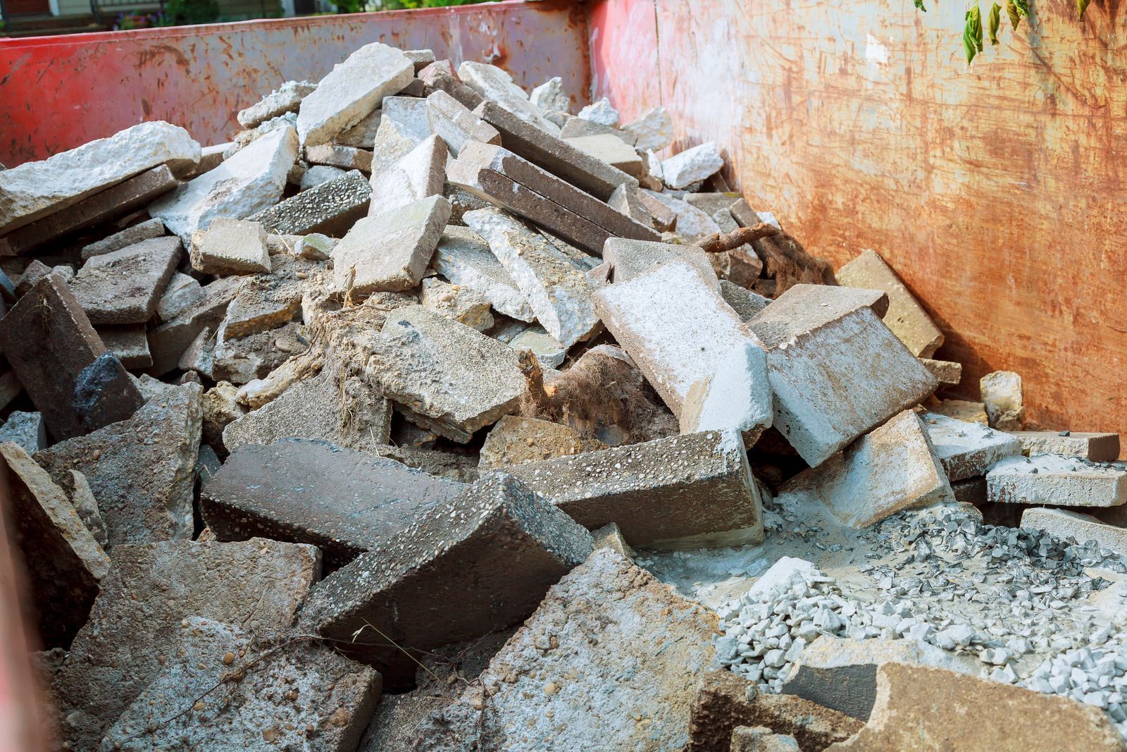 Chunks of broken concrete fill a rusty metal container.