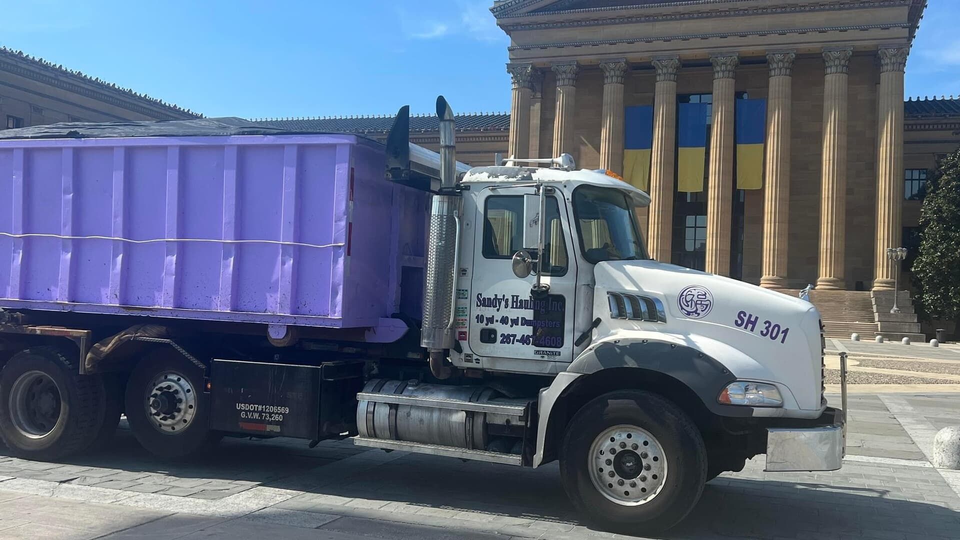 Purple dumpster truck parked in front of a large building with columns, Philadelphia Museum of Art.