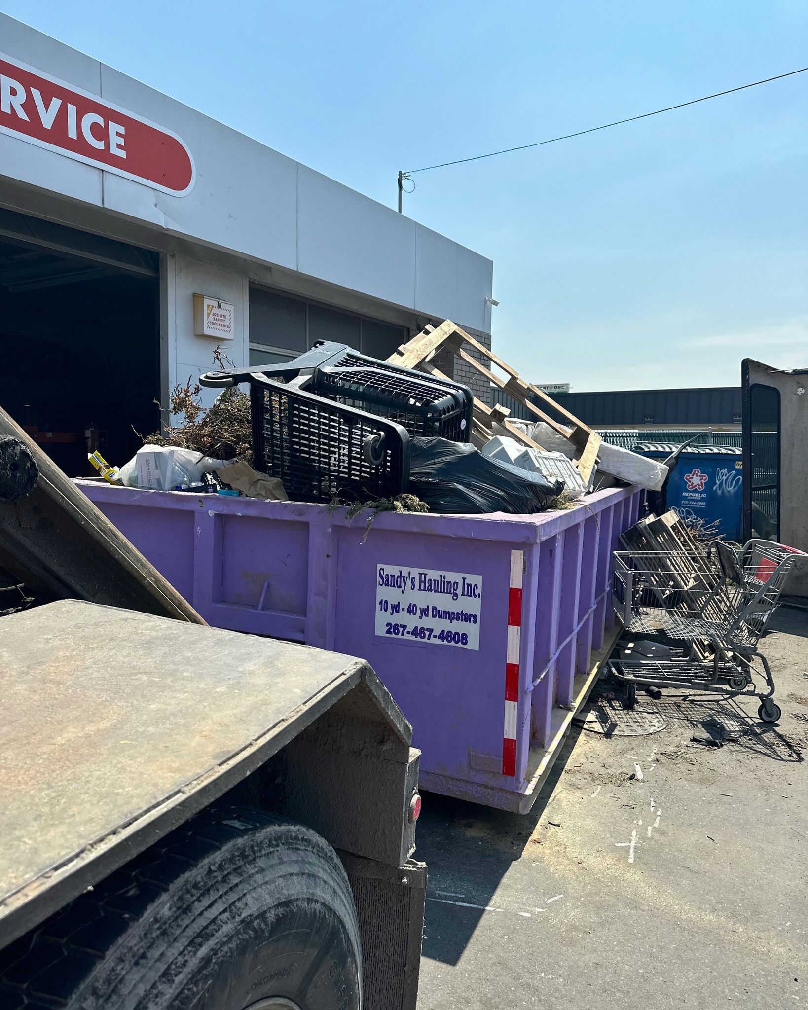 Green dumpster overflowing with scrap wood at a construction site.