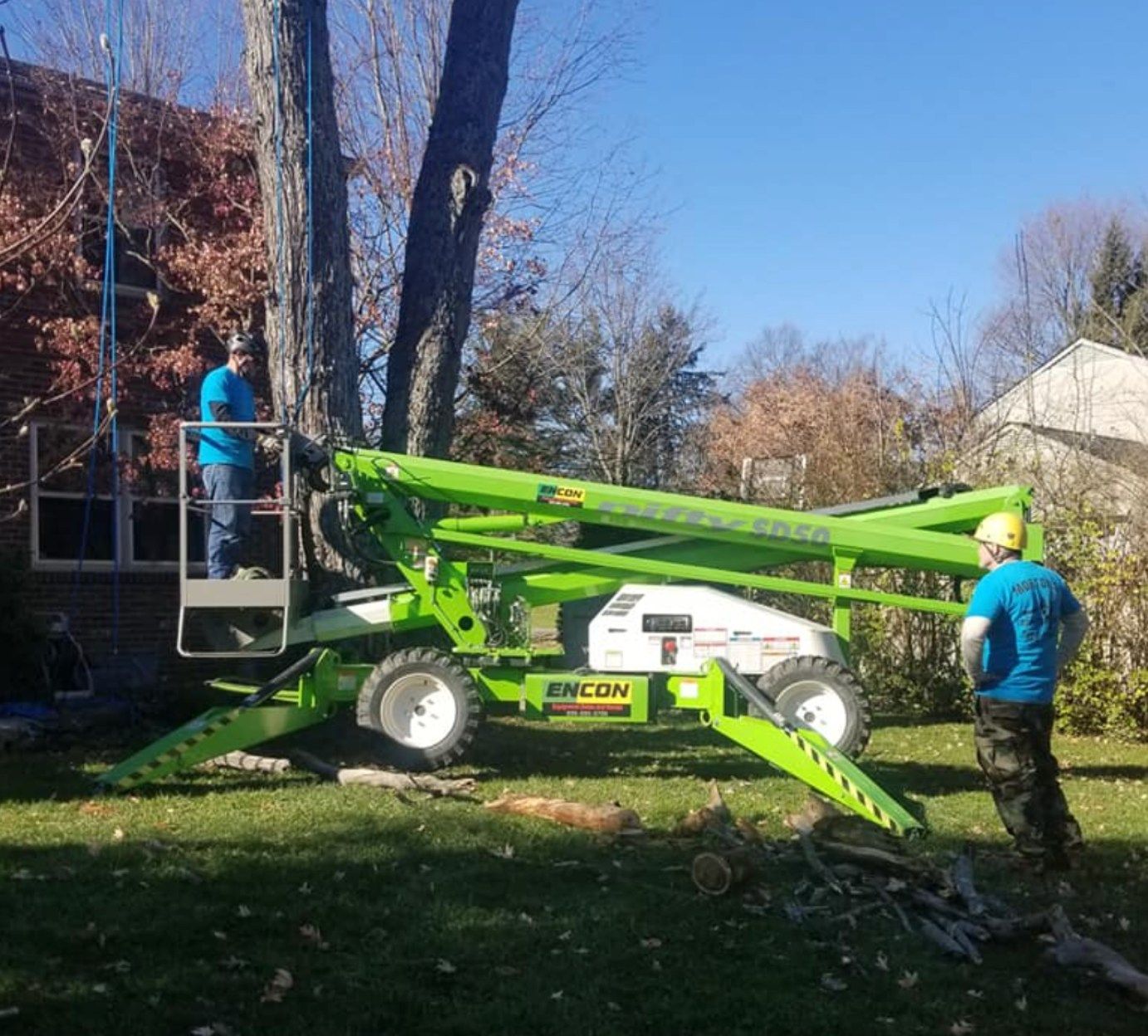 Two workers beside a green telescopic boom lift in a grassy yard on a sunny day