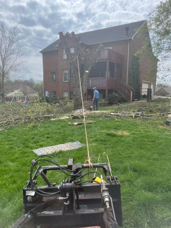 Lawn tractor in foreground facing a brick house, with a person near the porch and storm debris in the yard. Lawn tractor in foreground facing a brick house, with a person near the porch and storm debris in the yard.