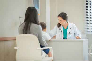 A woman is holding a baby while talking to a doctor.