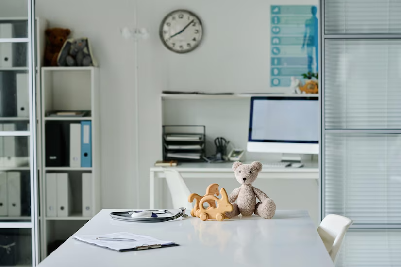 A teddy bear sits on a table in front of a computer