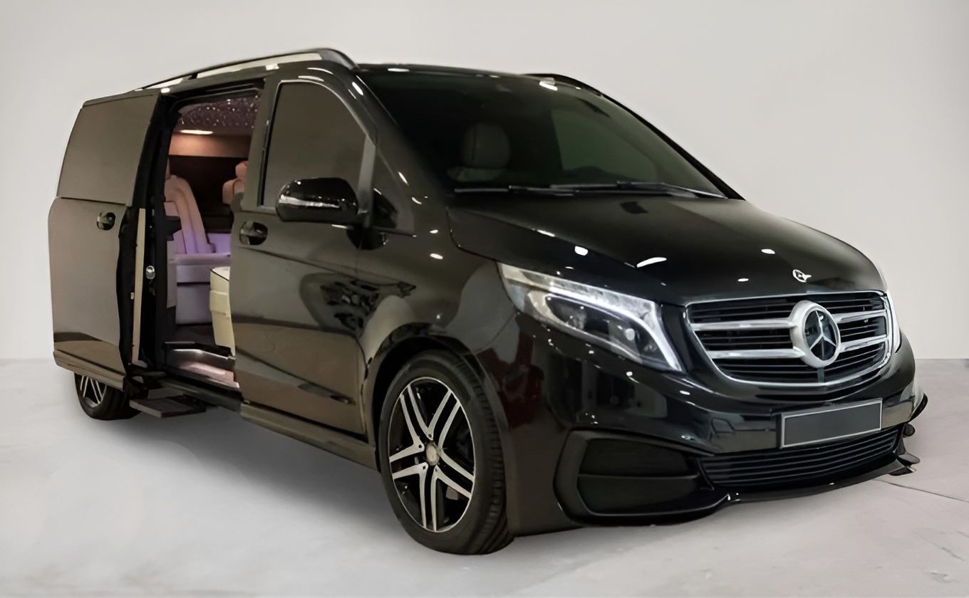 Un furgone Mercedes nero con le portiere aperte è parcheggiato su una superficie bianca.