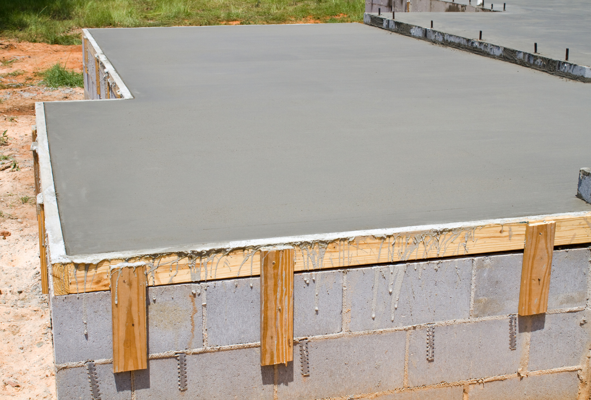 Newly poured concrete slab atop cinder block foundation, outdoor setting.
