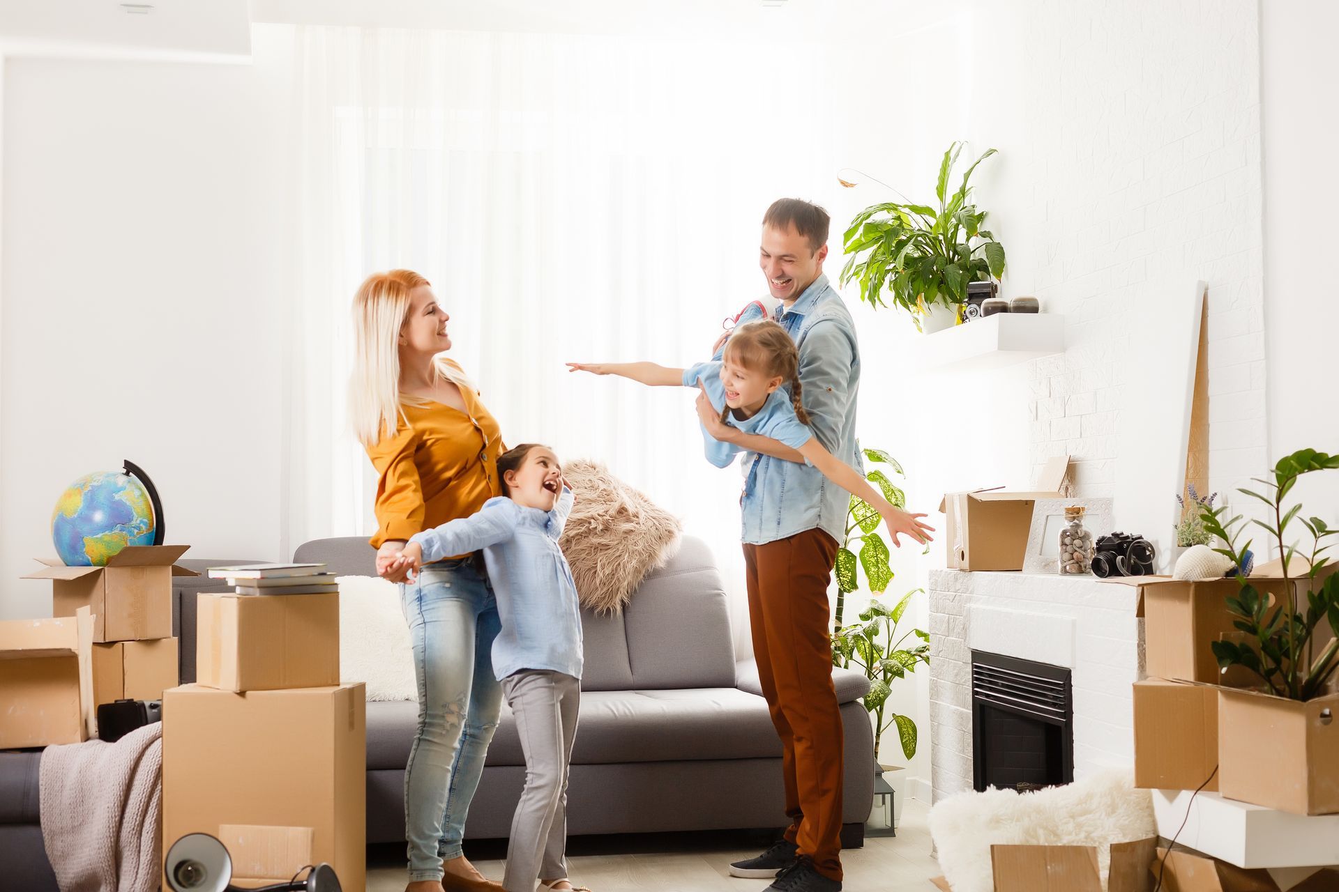 A family is standing in a living room surrounded by cardboard boxes.