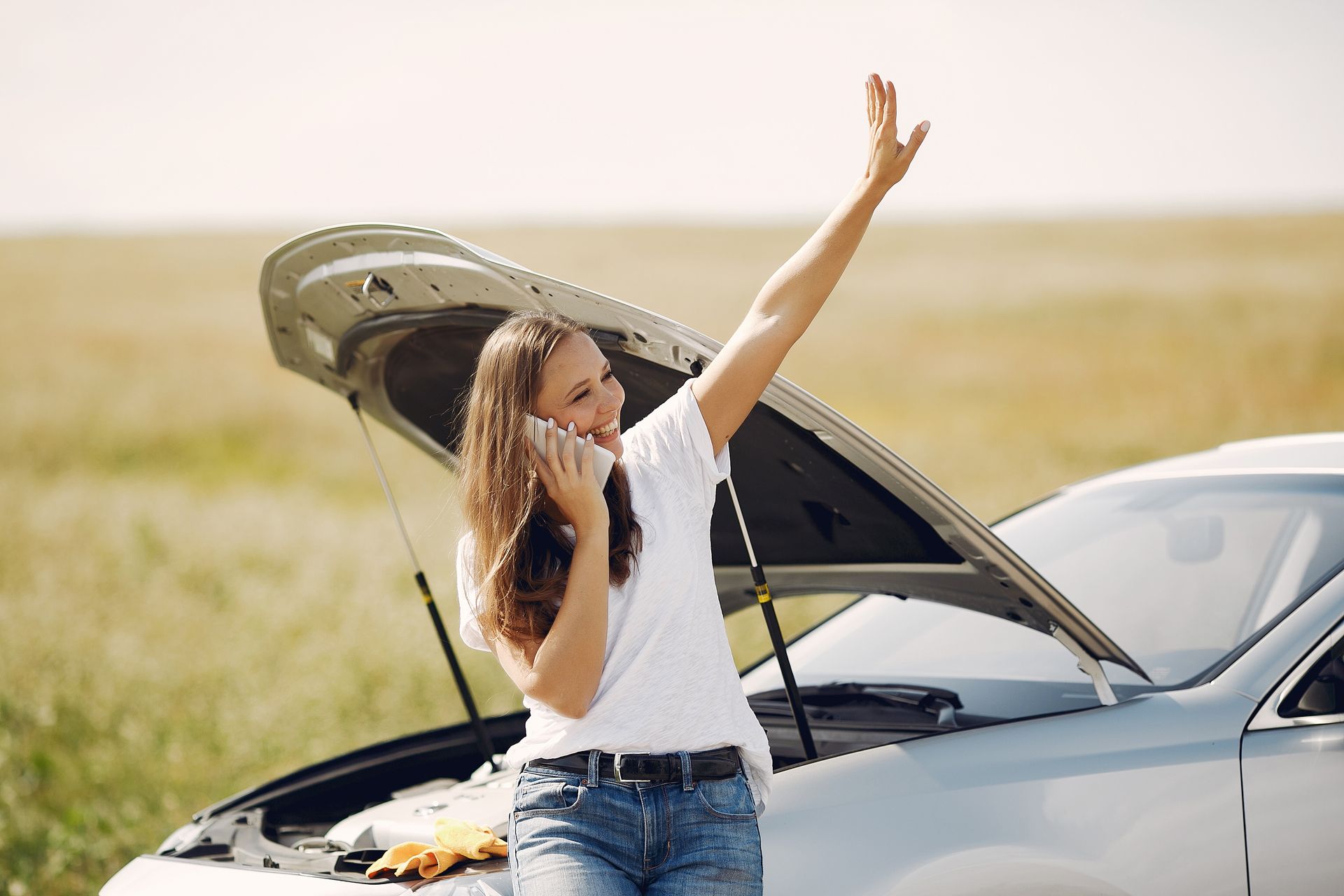 A woman is talking on a cell phone next to a broken down car.