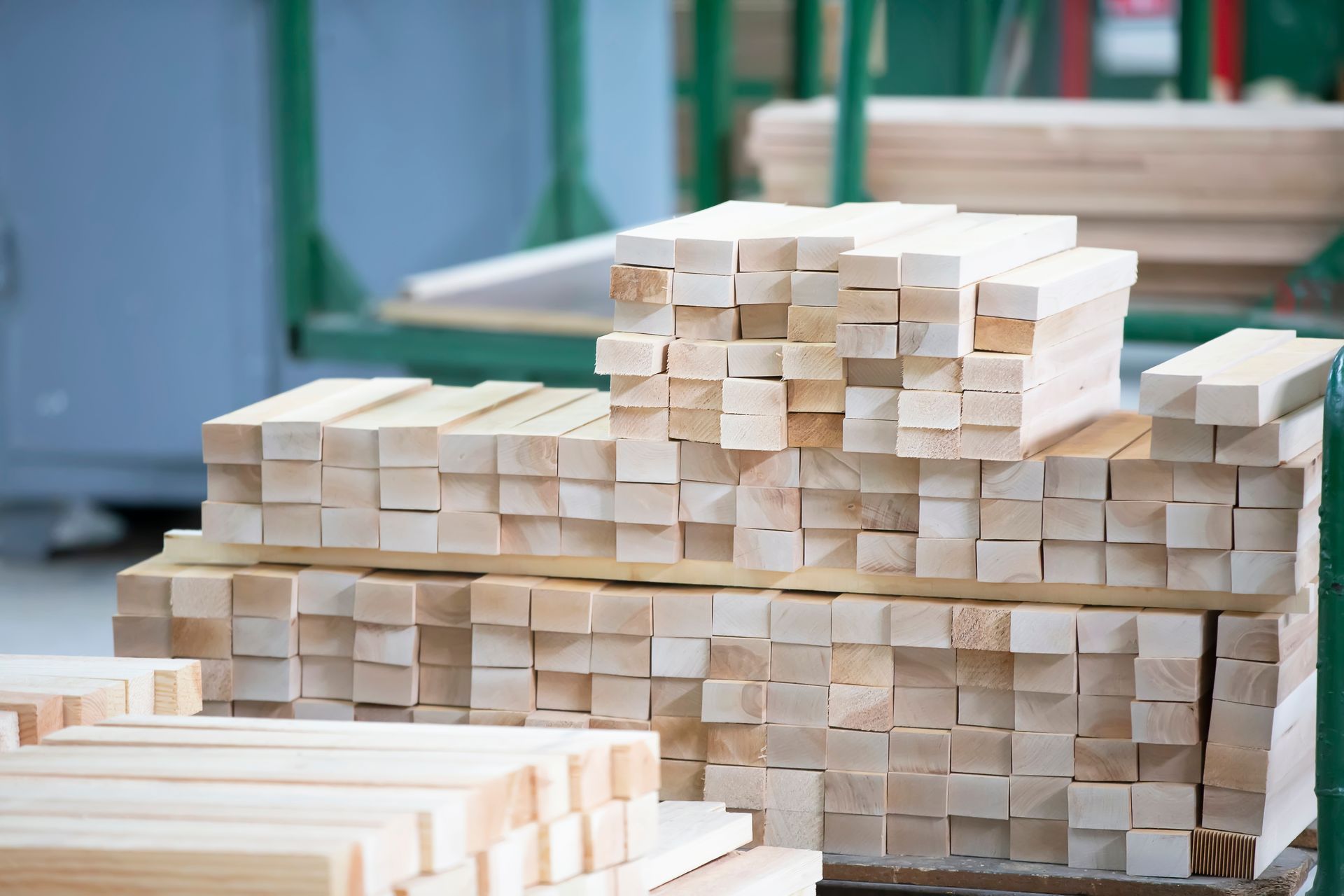 A stack of light-colored wooden beams neatly organized in a workshop or industrial storage setting. A stack of light-colored wooden beams neatly organized in a workshop or industrial storage setting.