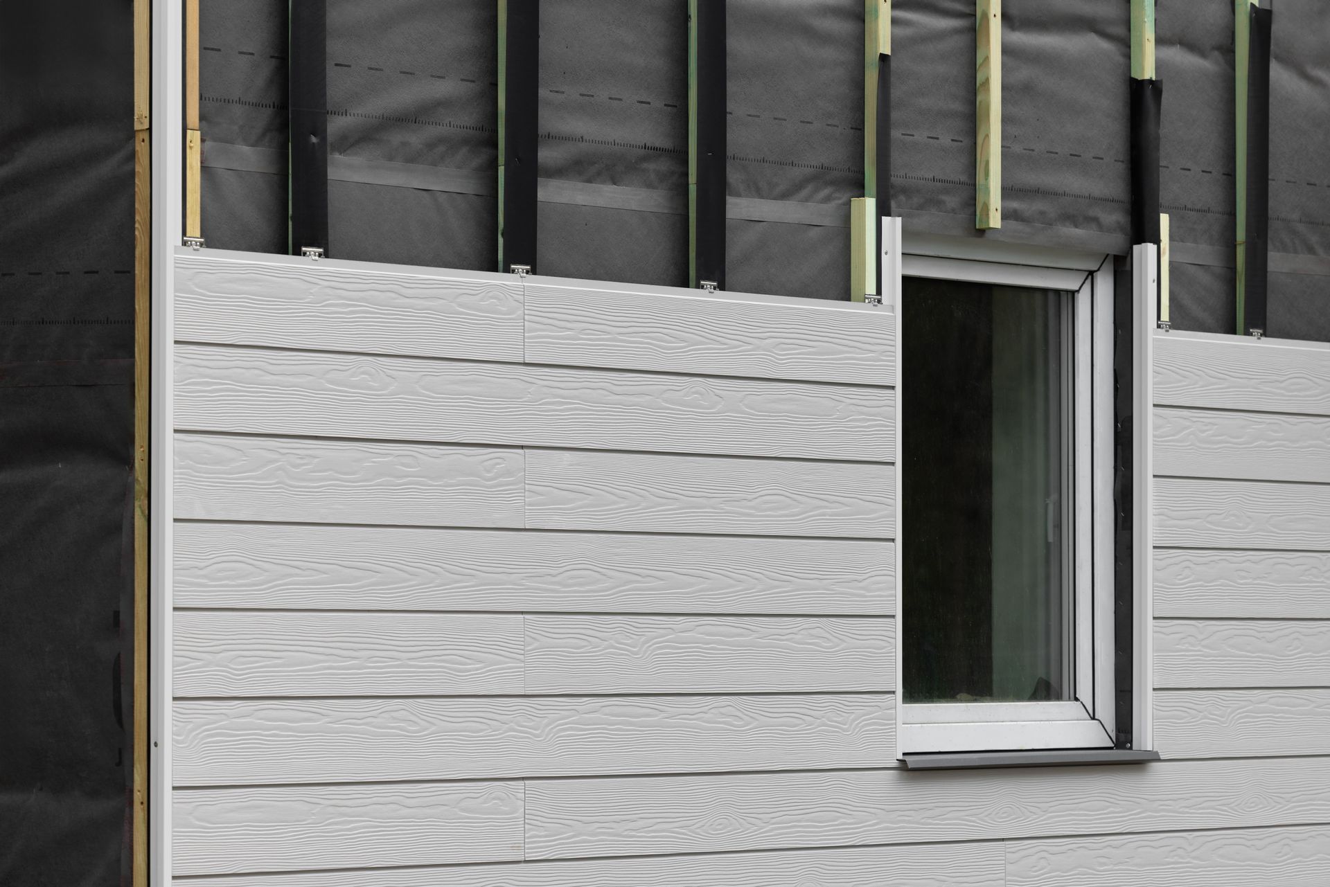 Light gray wood-grain siding being installed on the exterior of a building around a window.