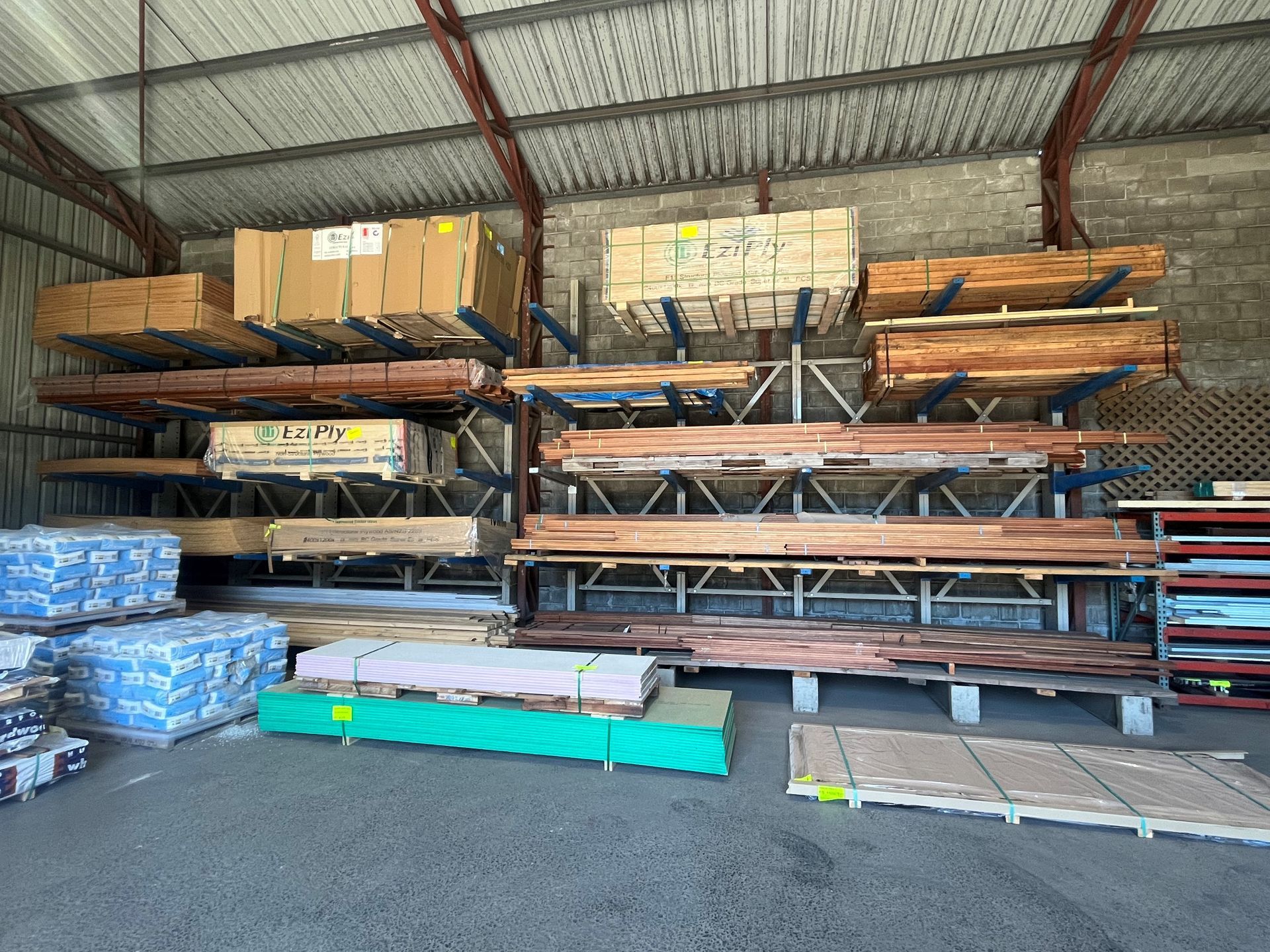 Wooden boards and sheet materials stacked on industrial metal racking in a warehouse storage facility.