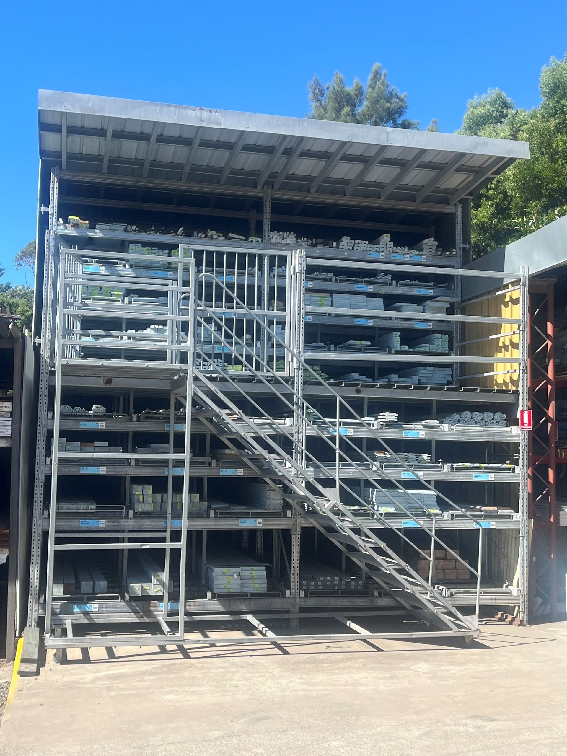 A large, multi-level metal industrial storage rack with built-in stairs and a catwalk, standing outdoors under a blue sky.