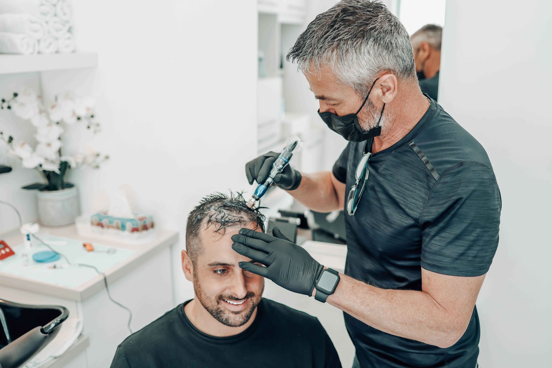 Un praticien portant un masque et des gants utilise un outil sur le cuir chevelu d'un client lors d'un traitement capillaire