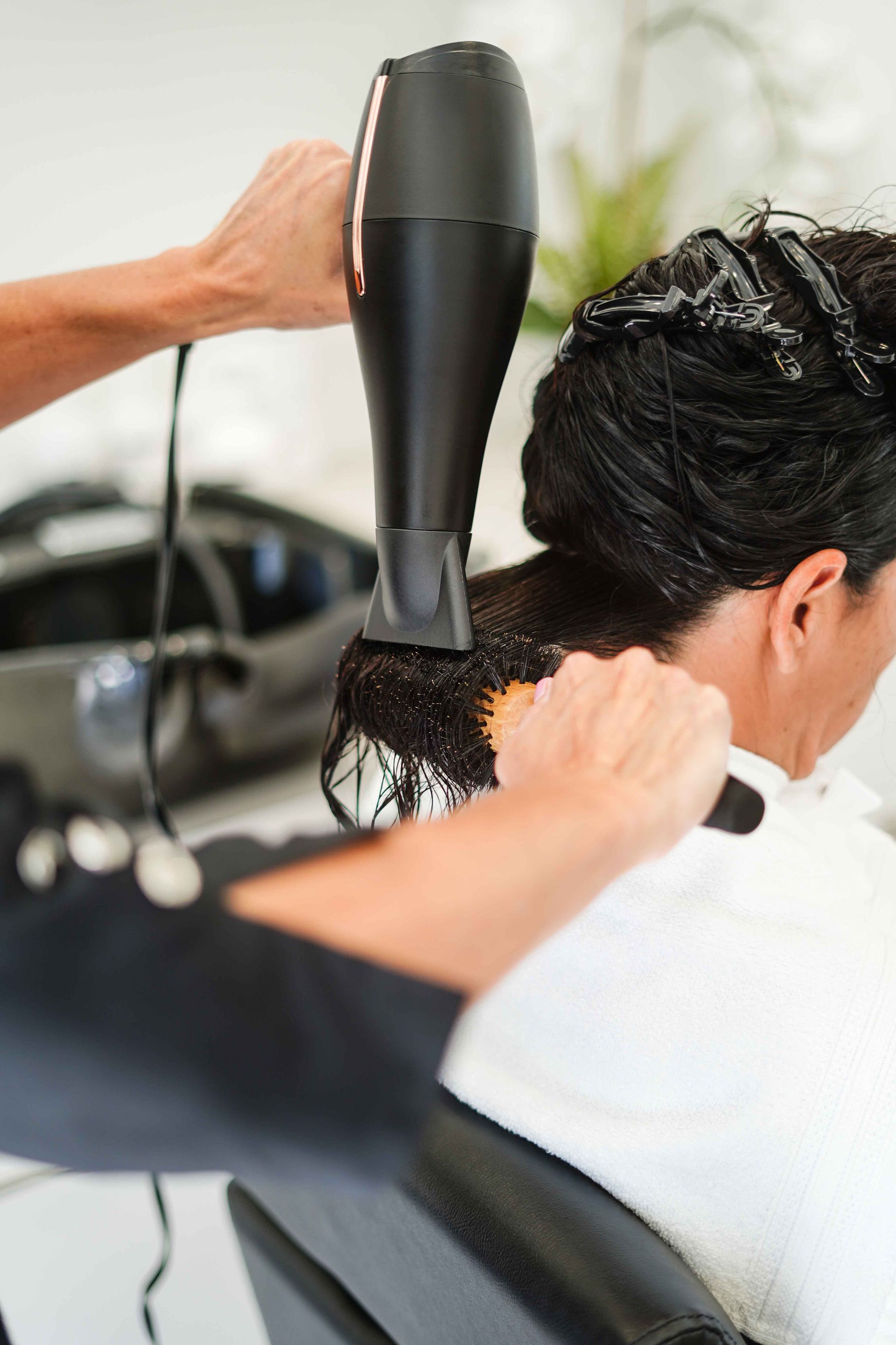 Hairdresser blow-drying a client's wet hair with a black hair dryer in a salon.