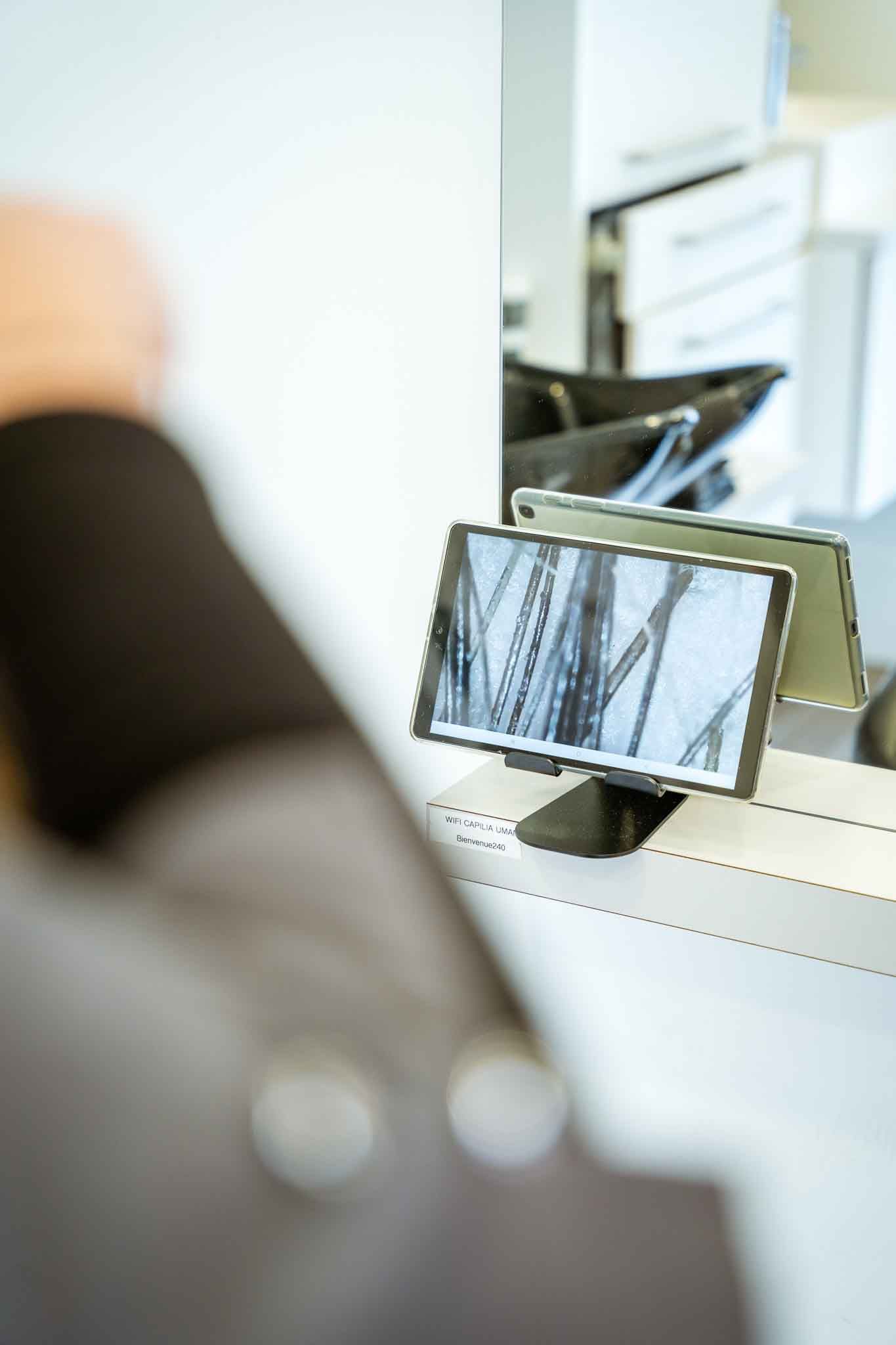 Person at a salon looking at a screen displaying a close-up of hair, reflected in a mirror.