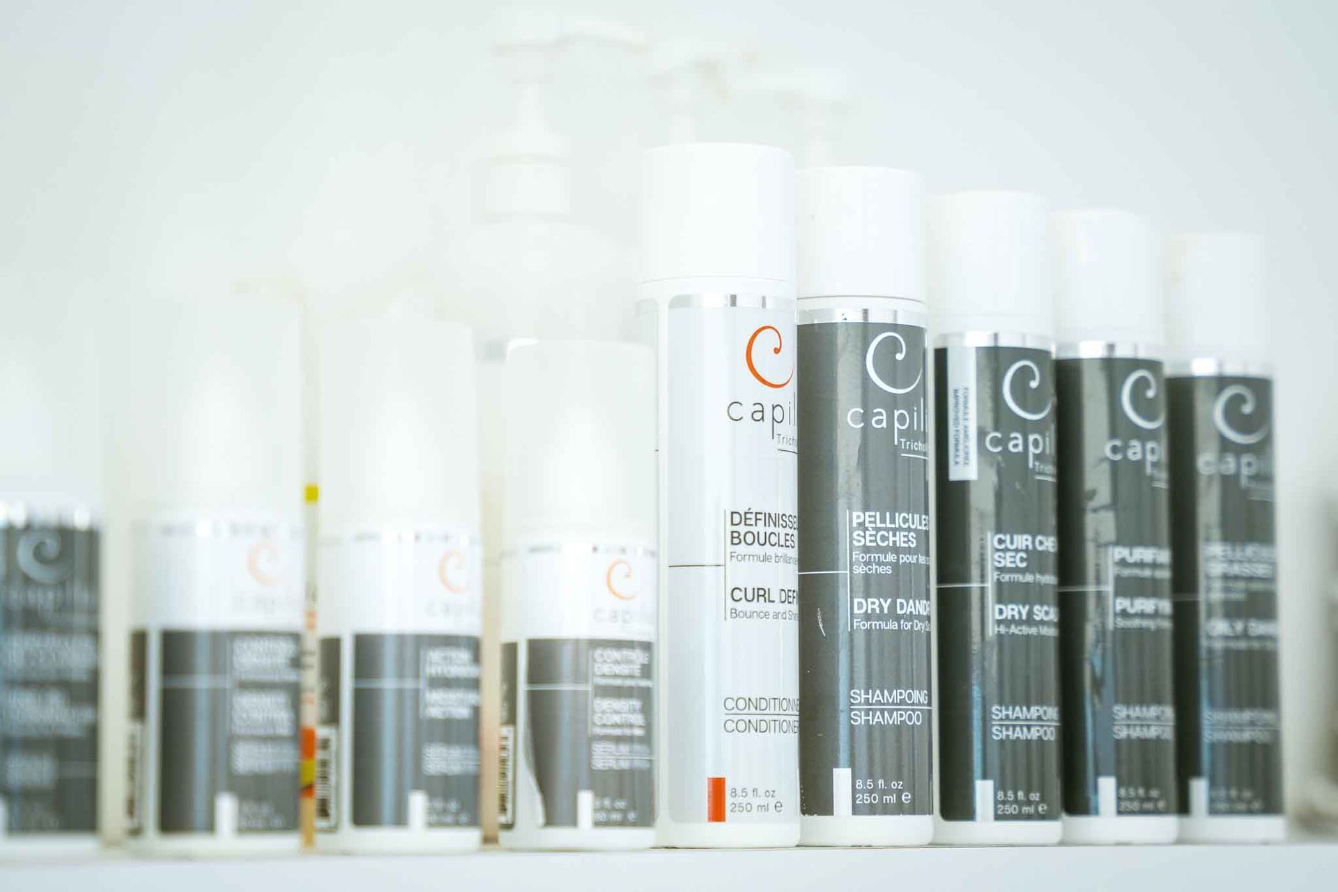 Row of white and silver hair product bottles with black labels on a shelf.