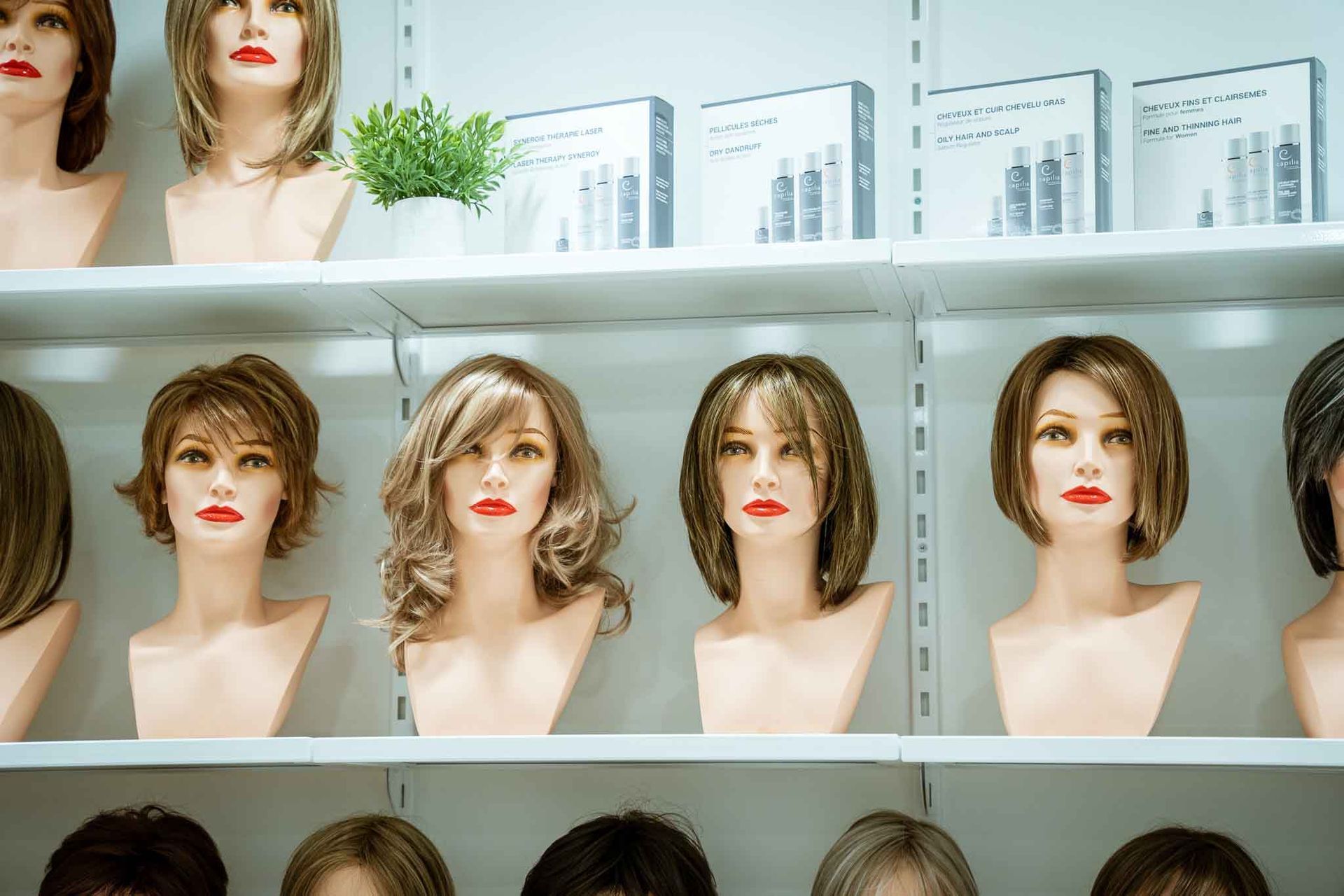 Des étagères d'exposition dans un magasin présentent différentes têtes de mannequins portant des perruques en cheveux synthétiques de styles variés.