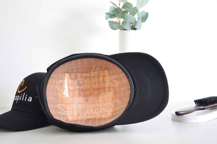 Black baseball cap with an open copper-colored interior, next to another black cap and a small brush.