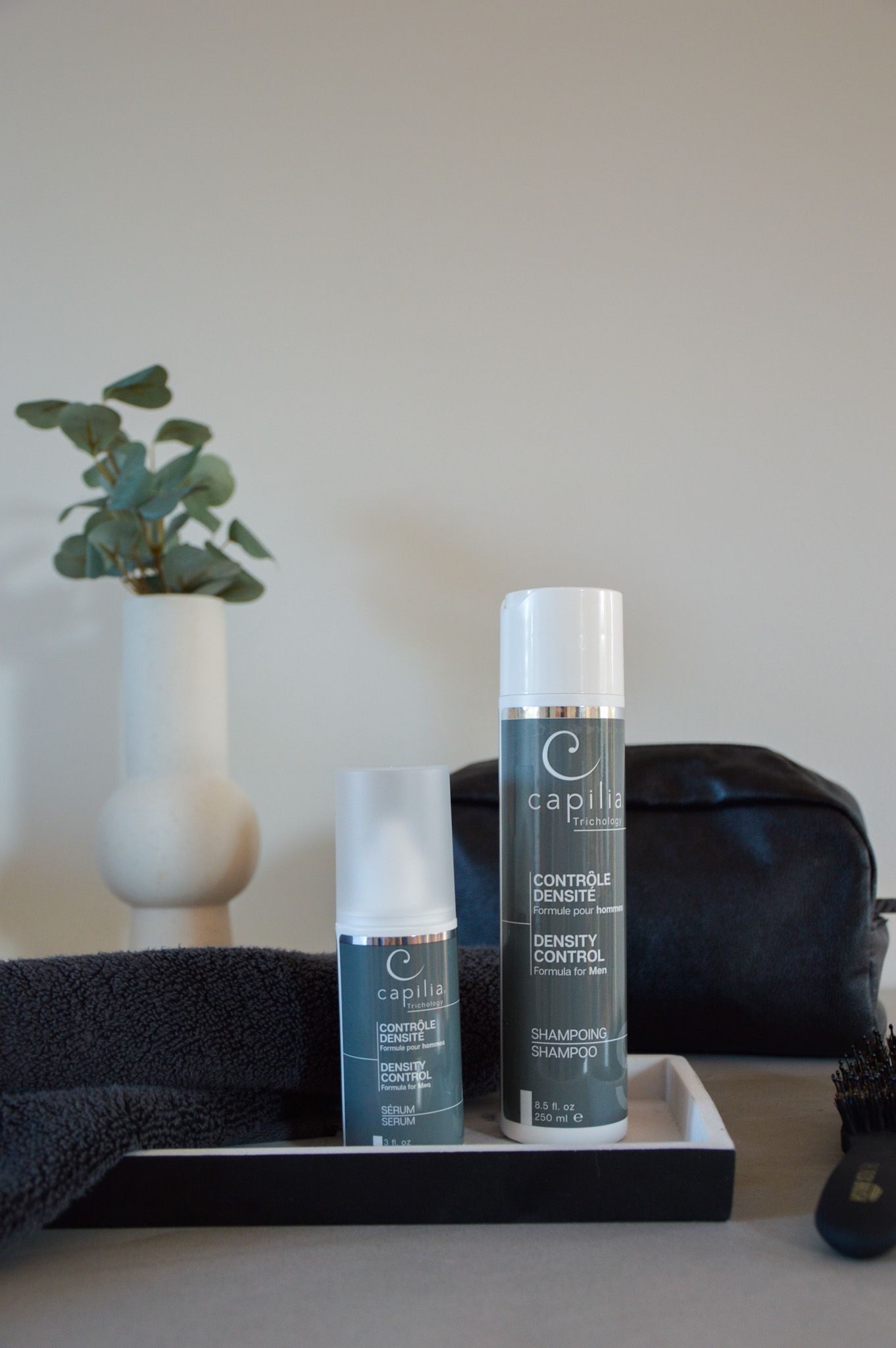 Skincare products on a tray with a towel, vase with plant, and toiletry bag.