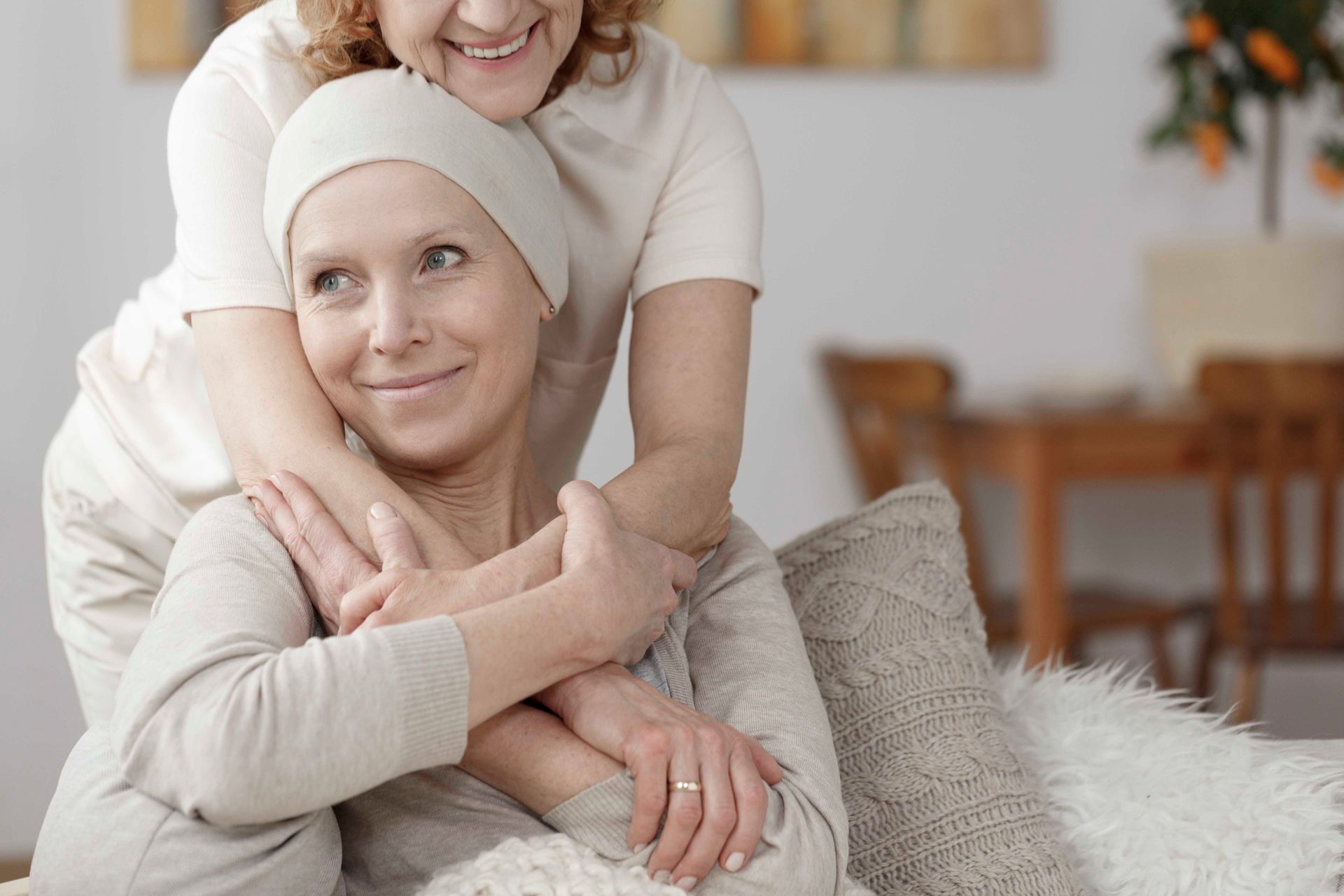 Woman with head covering smiles as another woman embraces her.
