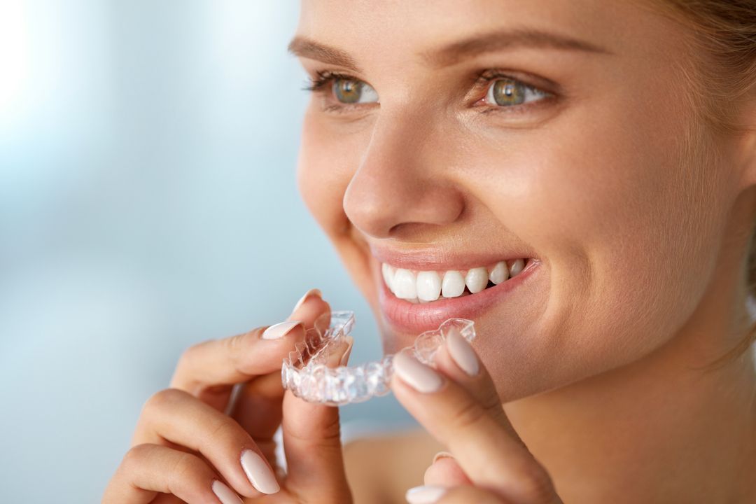 Smiling woman holding clear dental aligners near her mouth