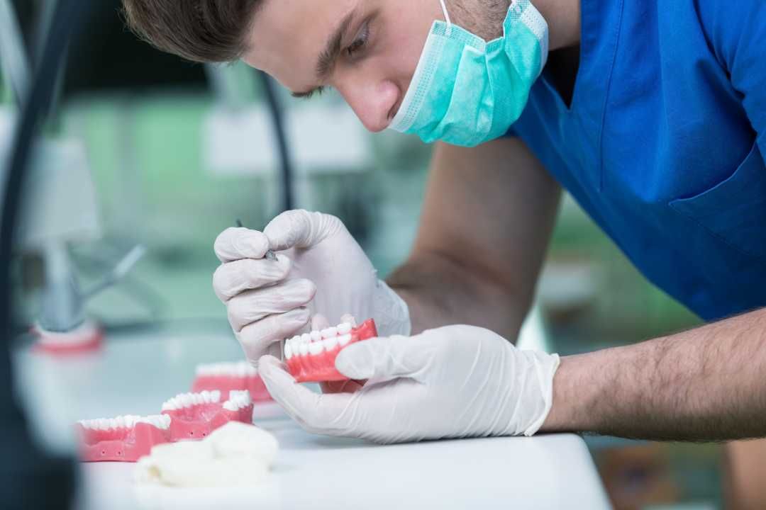Gloved technician inspecting a red dental mold with a tool in a lab setting