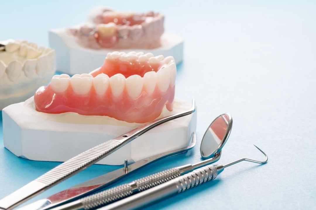 Dental dentures and metal dental tools on a light blue surface