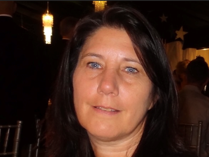 A woman with long dark hair and blue eyes smiles for the camera