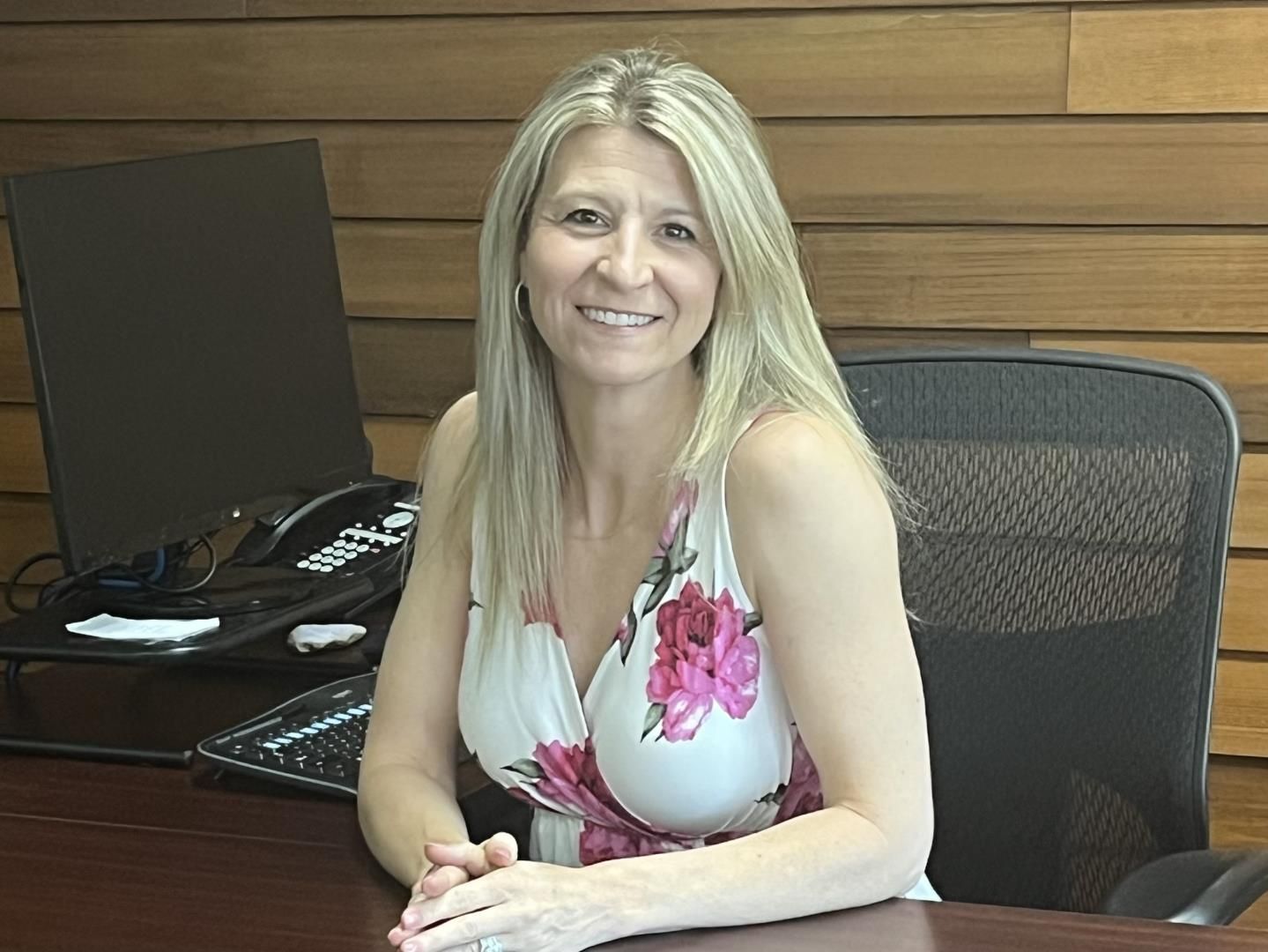 A woman is sitting at a desk in front of a computer and smiling.