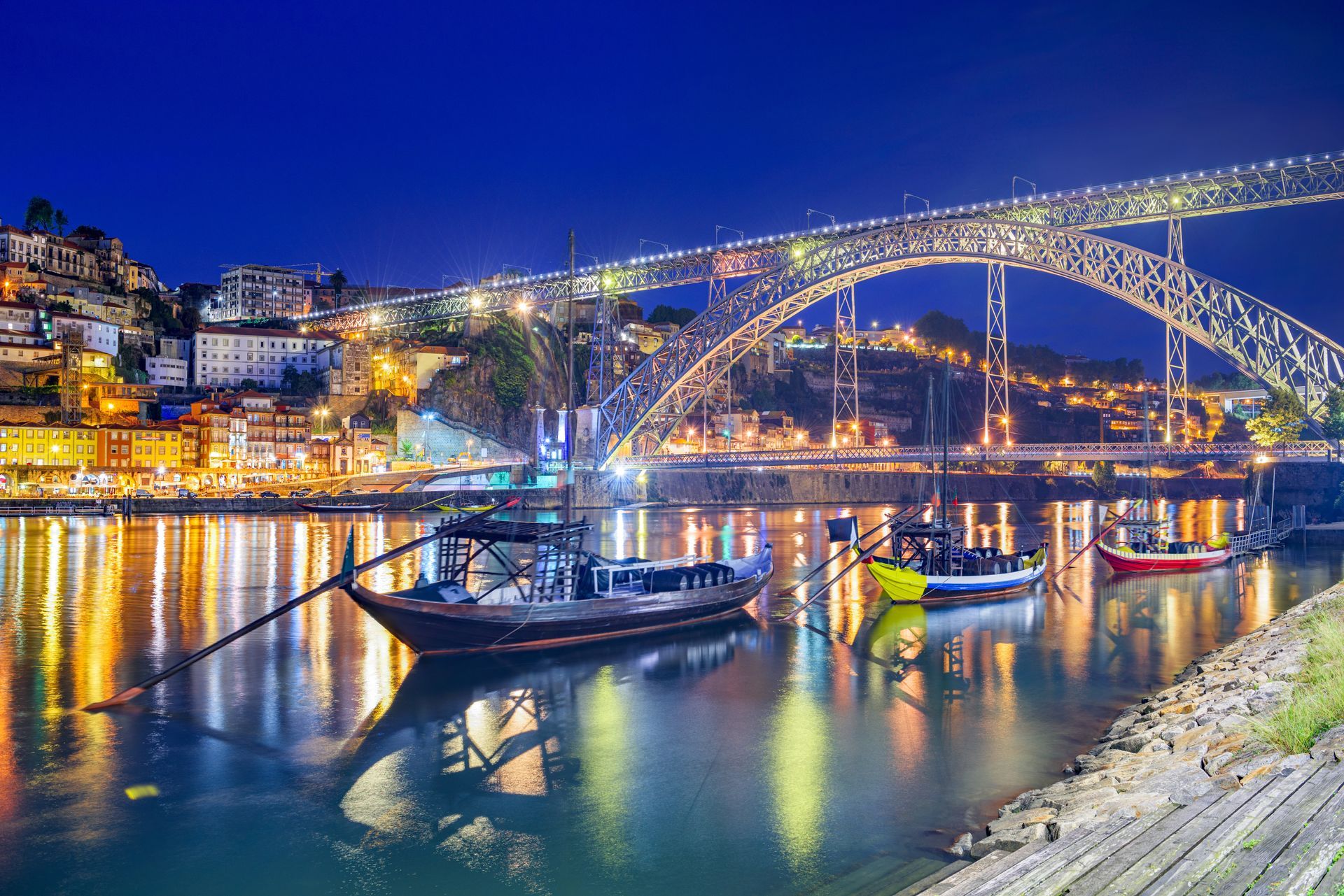 A bridge over a river with boats in the water at night.