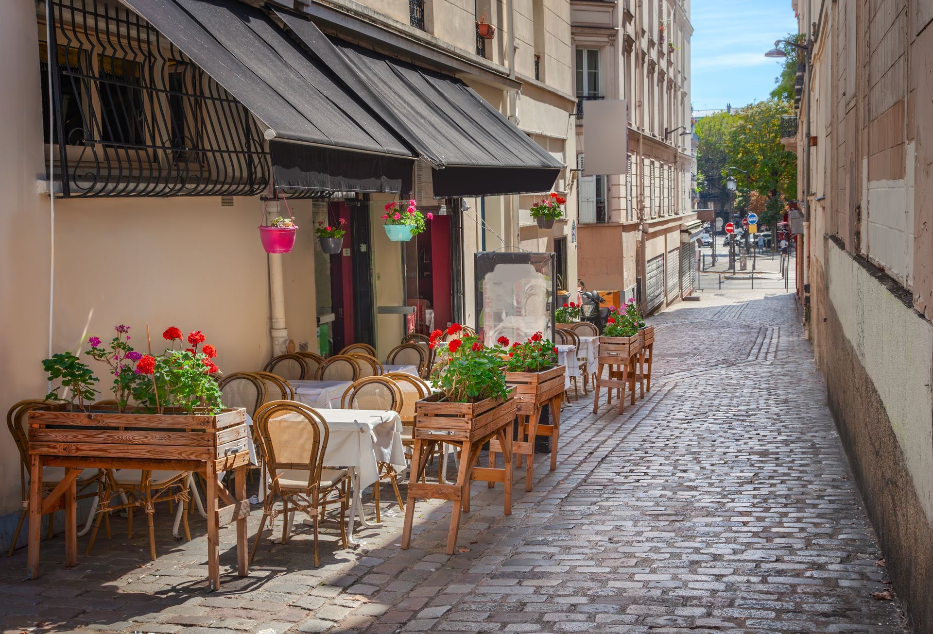 A cobblestone street with tables and chairs outside of a restaurant.