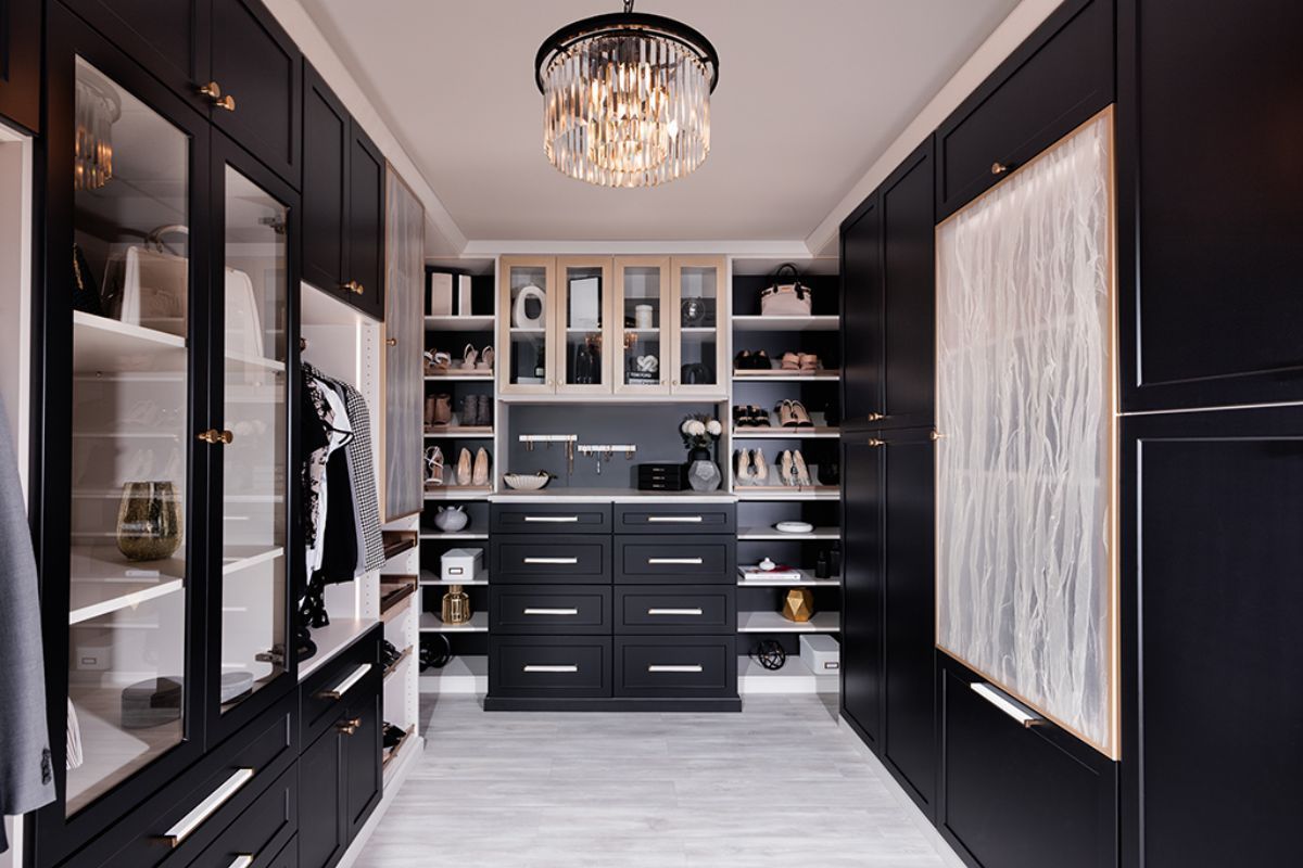 A walk in closet with black cabinets , drawers , shelves and a chandelier.