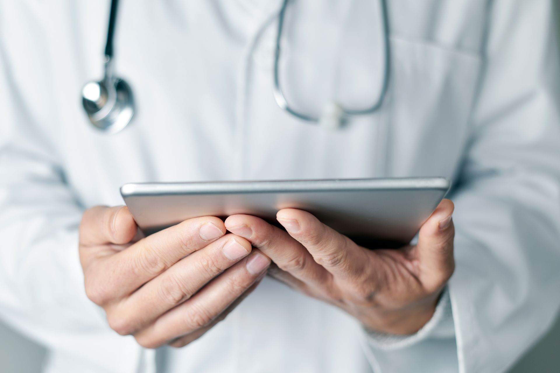 A doctor with a stethoscope around his neck is holding a tablet in his hands.