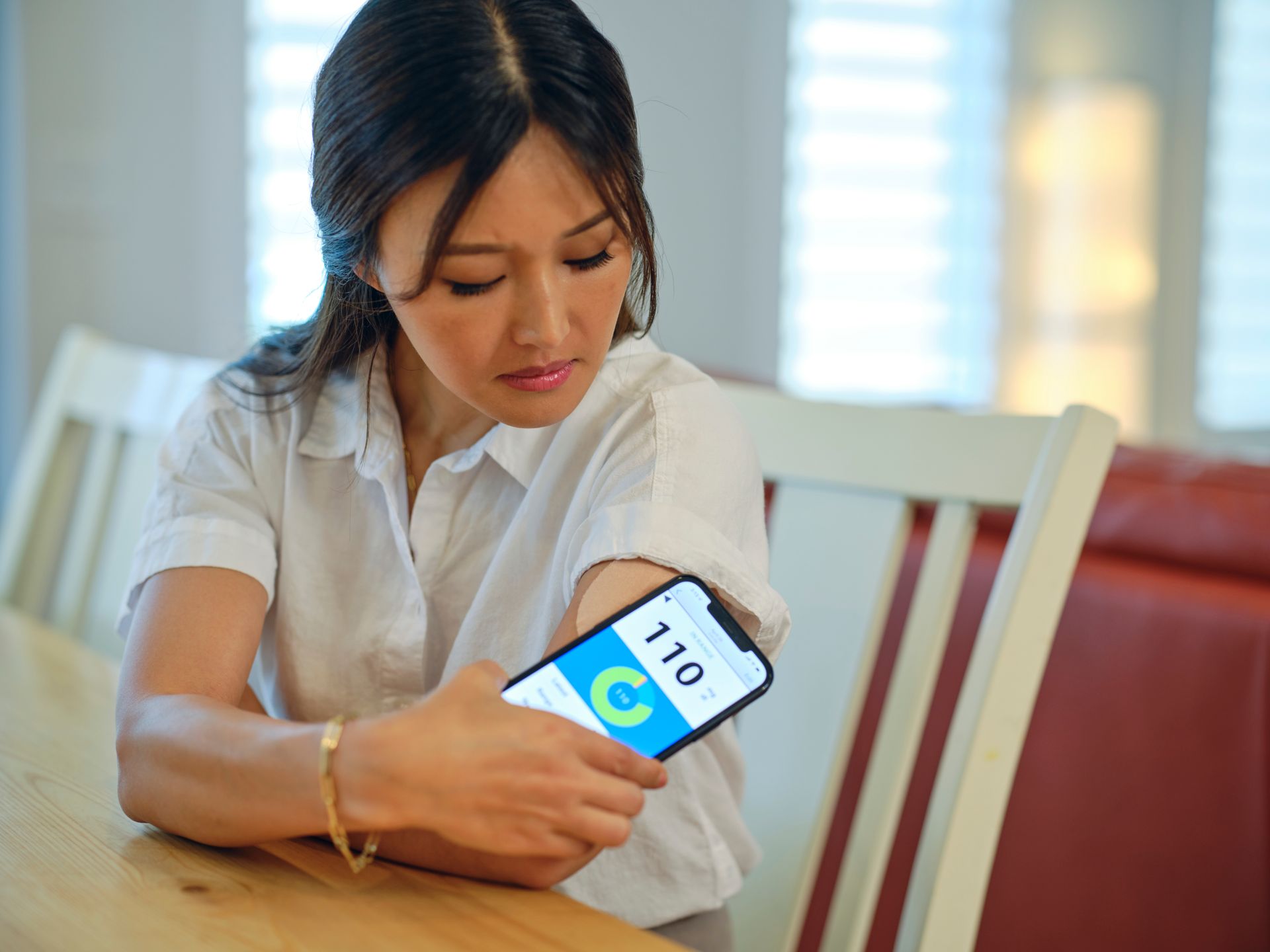 A woman is sitting at a table holding a cell phone in her hand.